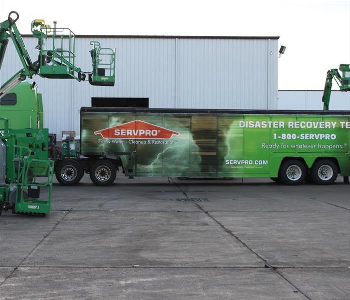 Green trucks and trailers in front of a commercial building.